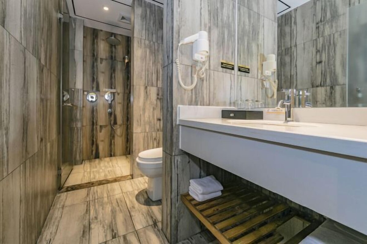 Un baño moderno con pared de mármol, inodoro blanco, ducha y tocador con espejo.