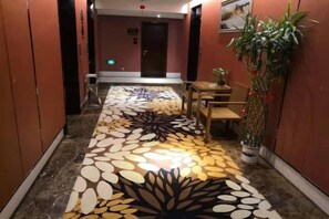 A hotel corridor with a patterned floor, a reception desk, and a potted plant. - Yongtai Gemini Holiday Hotel (Yongtai)