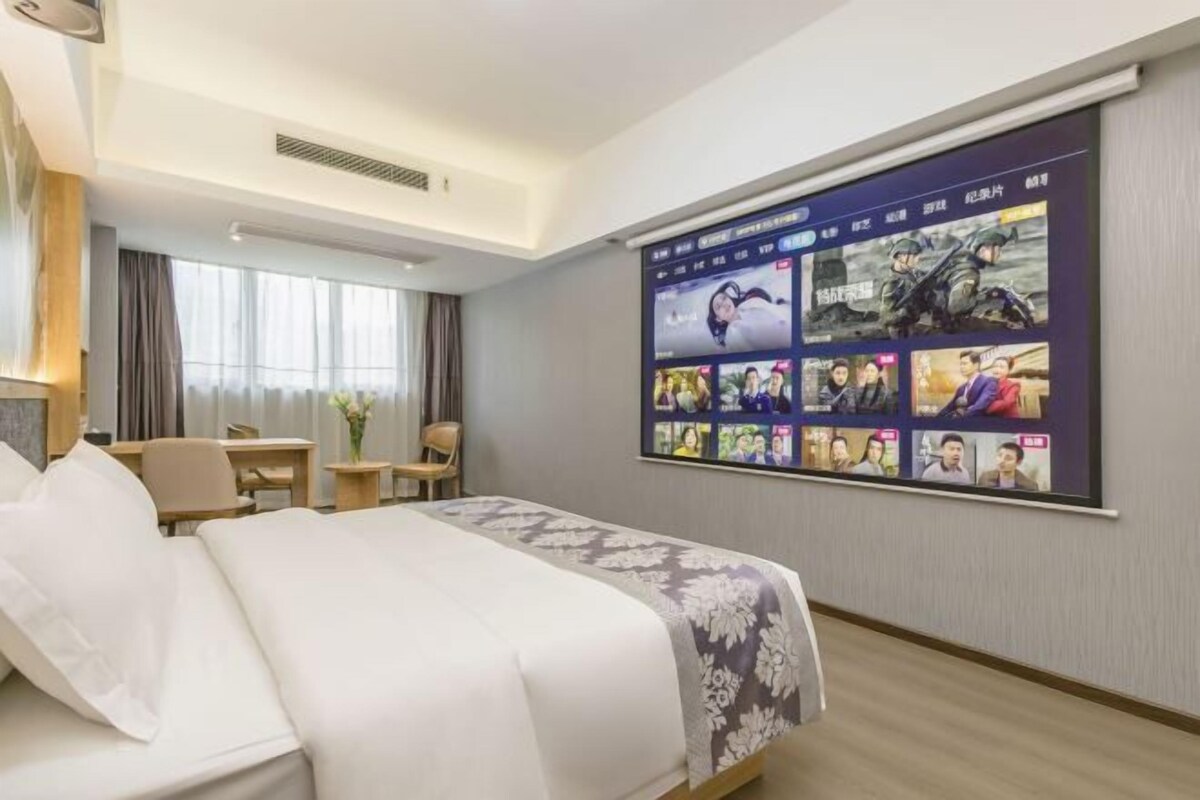 Una habitación de hotel con una cama grande, un escritorio, una silla y un televisor de pared mostrando varias imágenes.