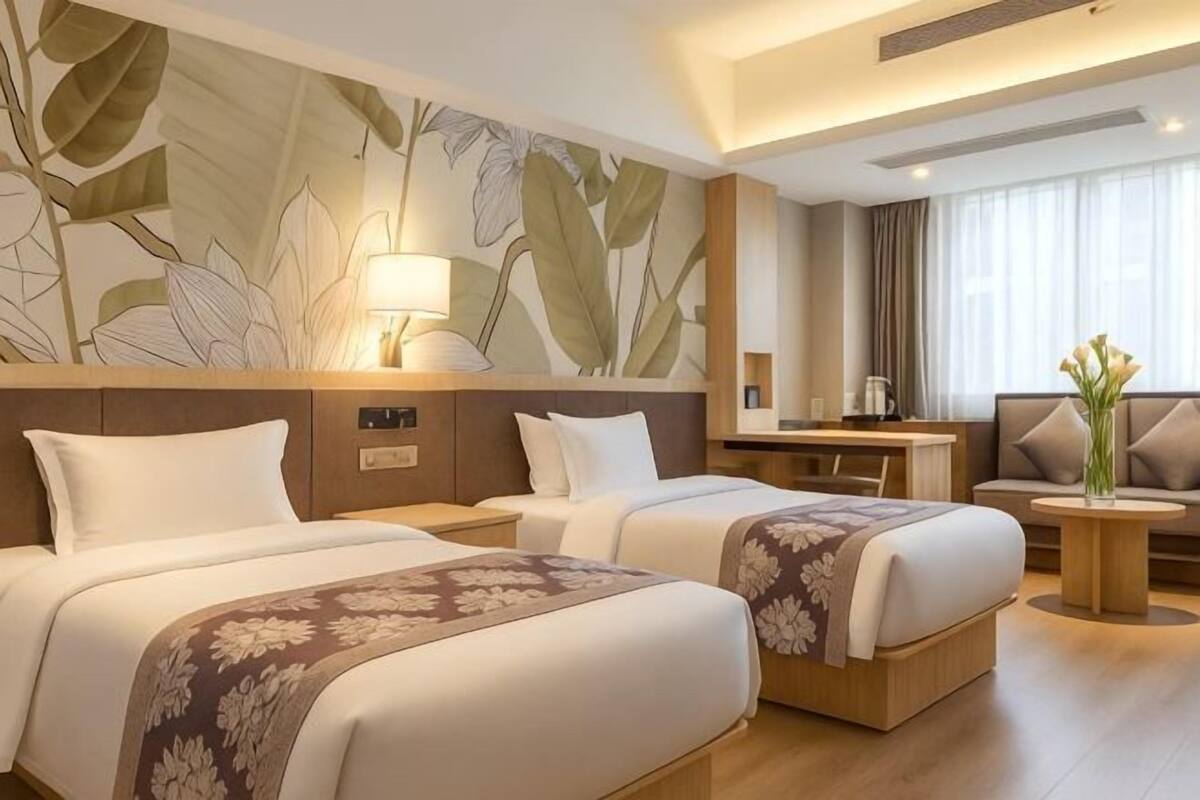 Habitació d'hotel amb dos llits, un escriptori, un sofà i una finestra gran amb cortines.