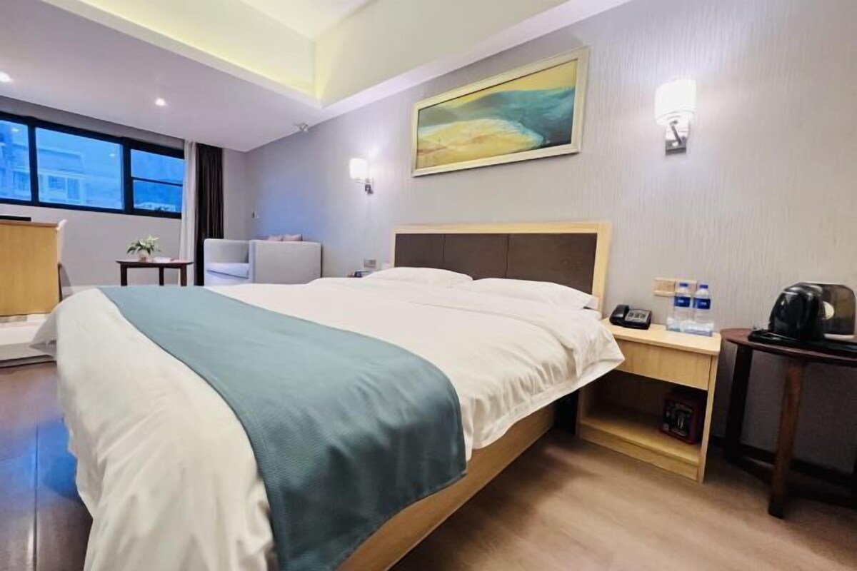 Una habitación de hotel con una cama grande, un escritorio con teléfono, una silla, una mesita con una planta y un cuadro en la pared.
