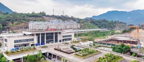 A modern building with a flat roof, surrounded by greenery and mountains in the background.