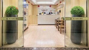 Un espace d’accueil doté d’un plancher en bois, d’un comptoir de réception, de deux plantes en pot et d’une enseigne avec la lettre « S ».