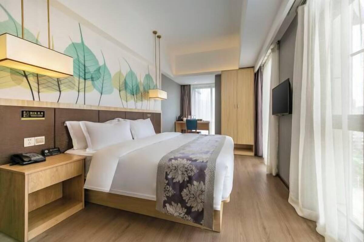 Habitació d'hotel amb llit, taula de nit, làmpada, obra d'art, televisió i cortines.