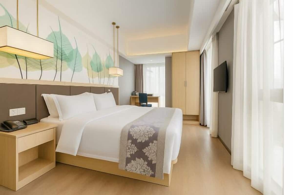 Una habitació d'hotel amb llit, taula de nit, làmpada, televisió i un quadre a la paret.
