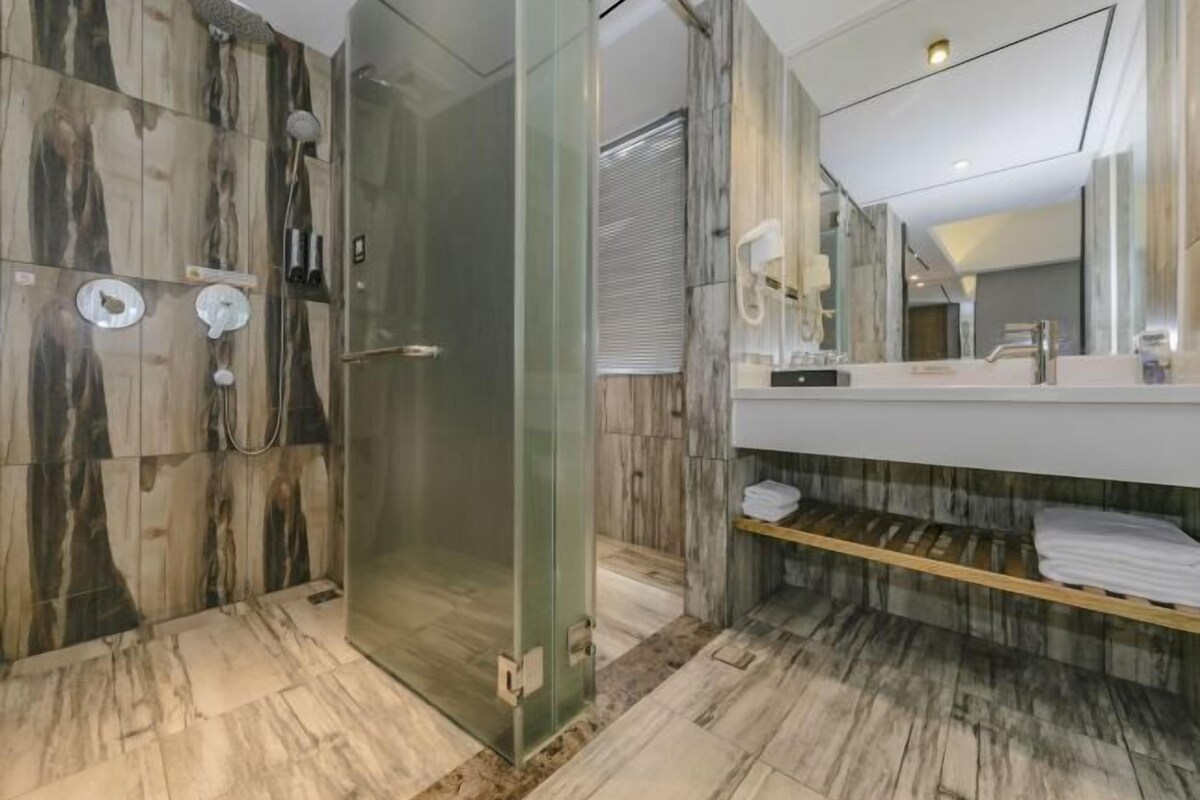 Un baño moderno con ducha envuelta en vidrio, paredes de mármol y tocador con espejo.