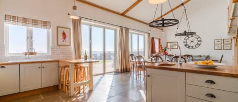 A modern kitchen with a large island, wooden beams, and a view to the outside.
