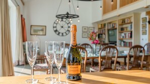 En flaska Canti Prosecco DOC och tre tomma vinglas står på ett träbord i ett väl upplyst rum. På väggen hänger en stor klocka och i bakgrunden syns bokhyllor.