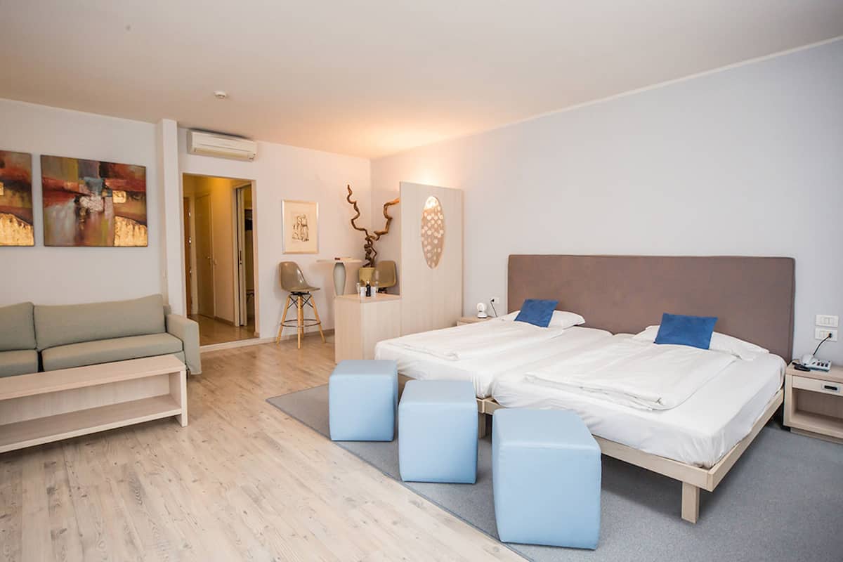 Una habitación de hotel moderna con una cama grande, dos mesitas de noche, un sofá y un escritorio.