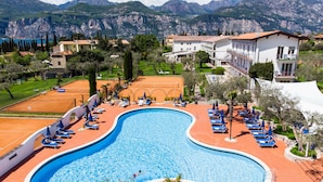 Une piscine entourée de bâtiments et de montagnes, avec des chaises longues et des parasols.