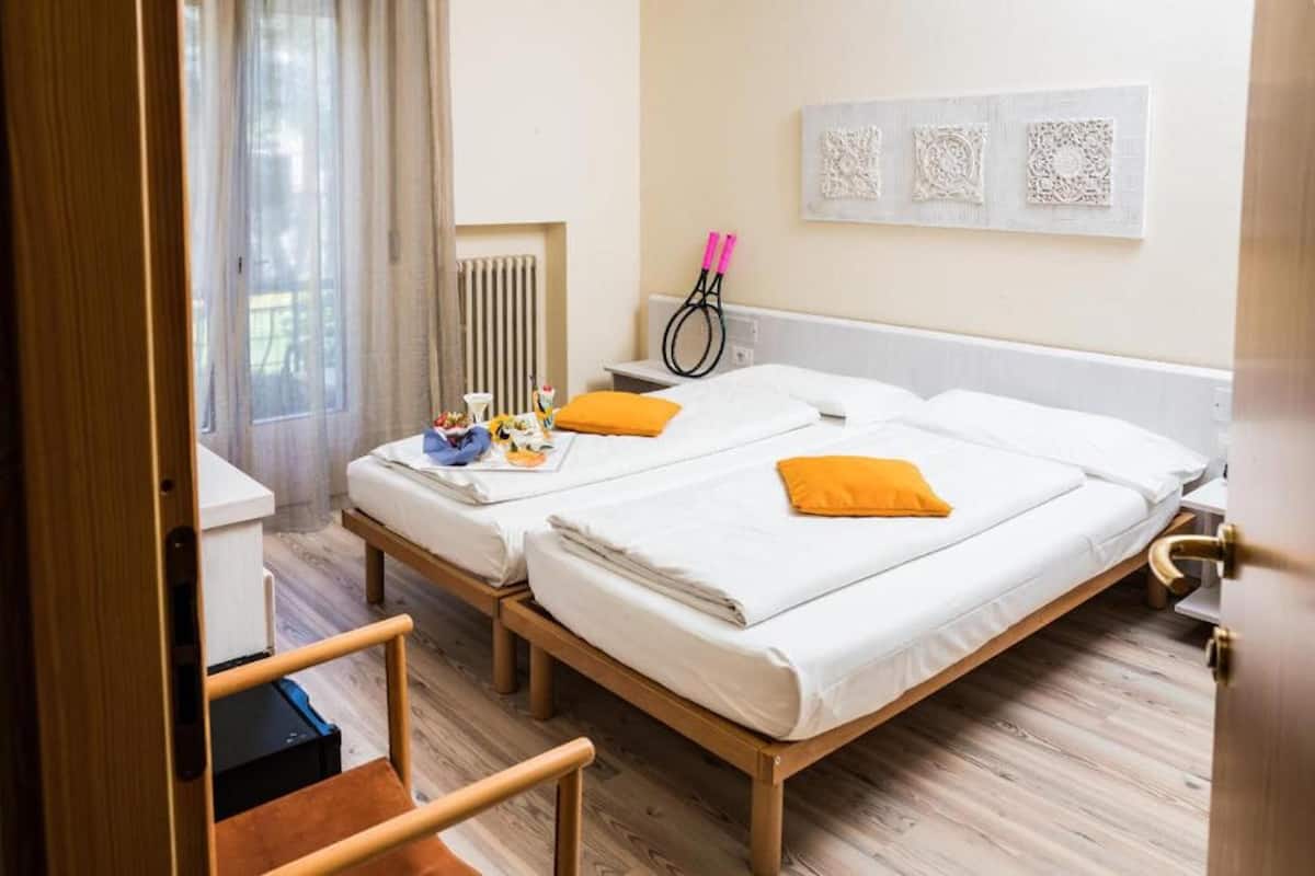 Habitación de hotel con dos camas, un radiador, un escritorio y una ventana con cortinas.