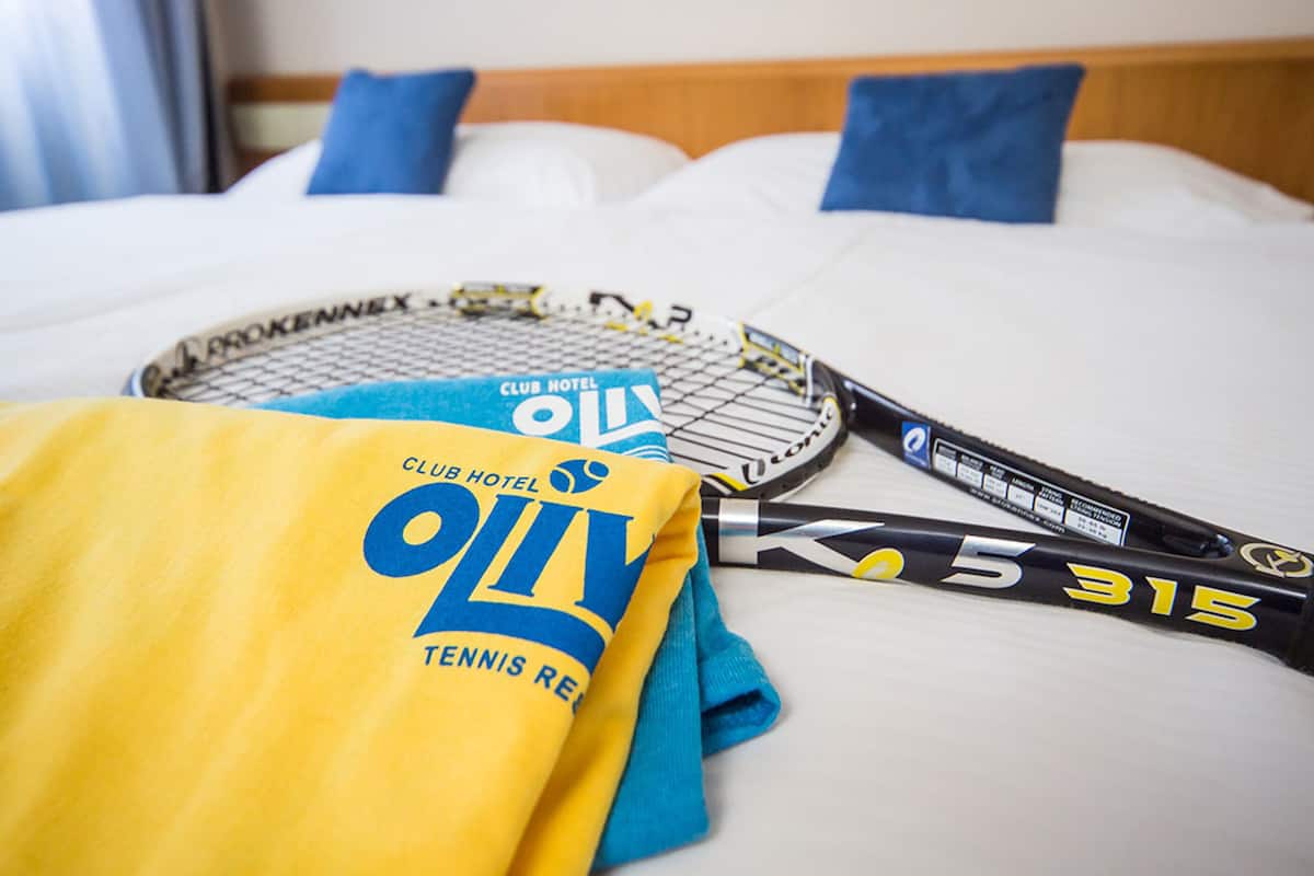 Una cama con sábanas blancas, almohadas azules y dos raquetas de tenis encima.