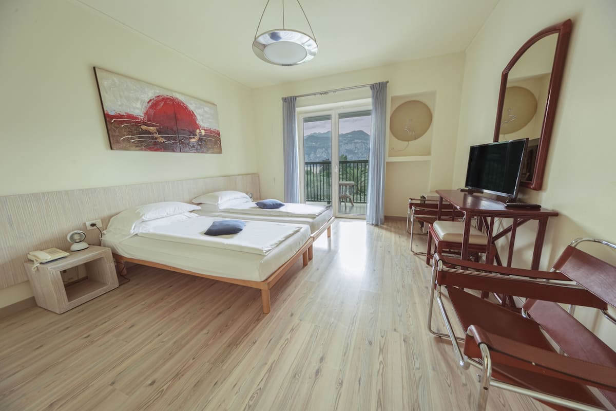Habitación de hotel con dos camas, televisión, escritorio y balcón con vistas a montañas.