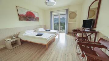 A hotel room with two beds, a TV, a desk, and a balcony with a view of mountains.