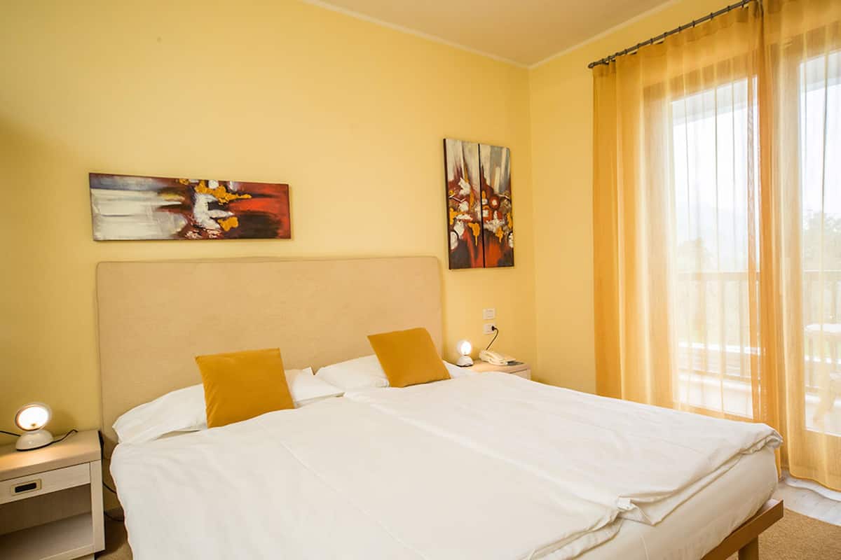 Habitación de hotel con una cama grande, dos almohadas, una mesita de noche con lámpara y obras de arte en las paredes.