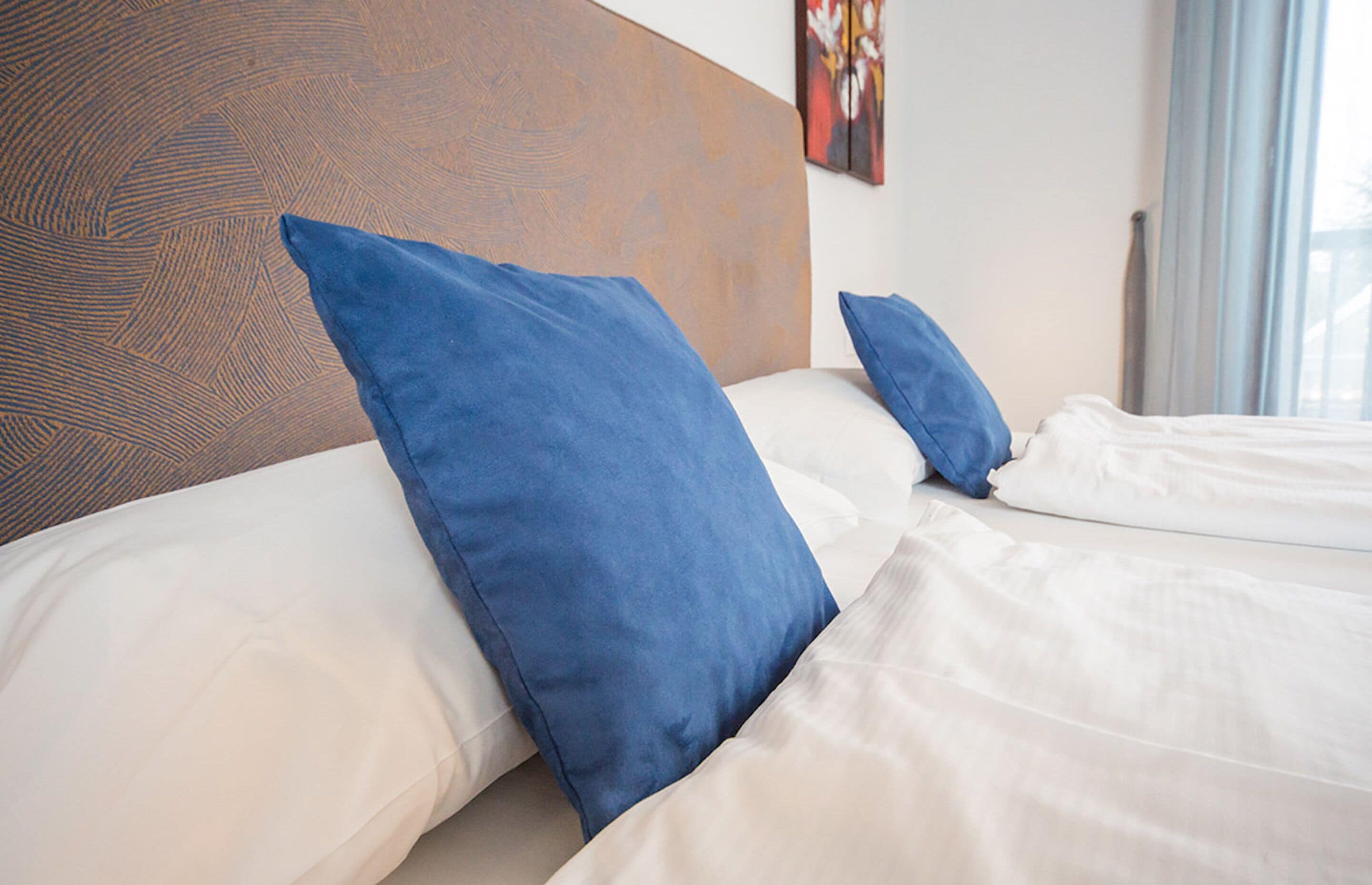 Una habitación de hotel con cabecera de madera, dos almohadas azules y ropa de cama blanca.