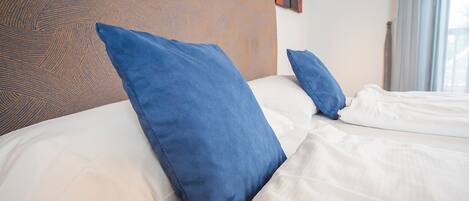 Una habitación de hotel con cabecera de madera, dos almohadas azules y ropa de cama blanca.