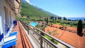 Un balcon offrant une vue sur un court de tennis, une piscine et un paysage montagneux.
