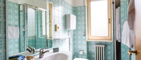 A bathroom with a sink, mirror, toilet, and a window.