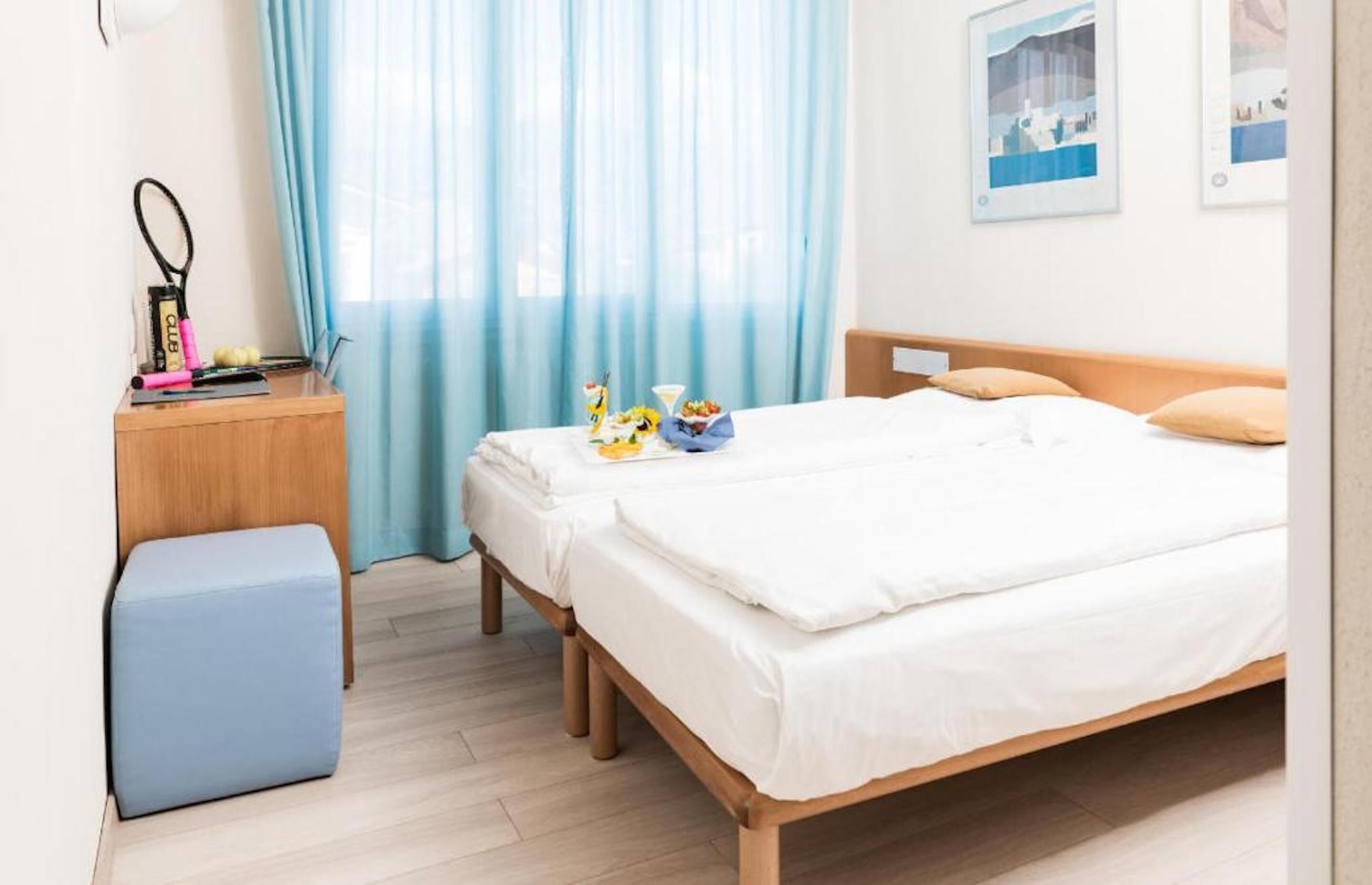 Ein Schlafzimmer mit einem Bett, einem Nachttisch mit Lampe, einem kleinen Hocker und einem Fenster mit Vorhängen.
