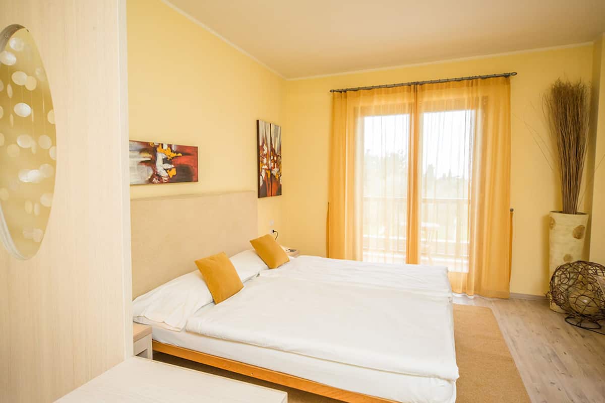 Habitación de hotel con una cama grande, dos almohadas, una mesita de noche, un cuadro en la pared y una ventana con cortinas.