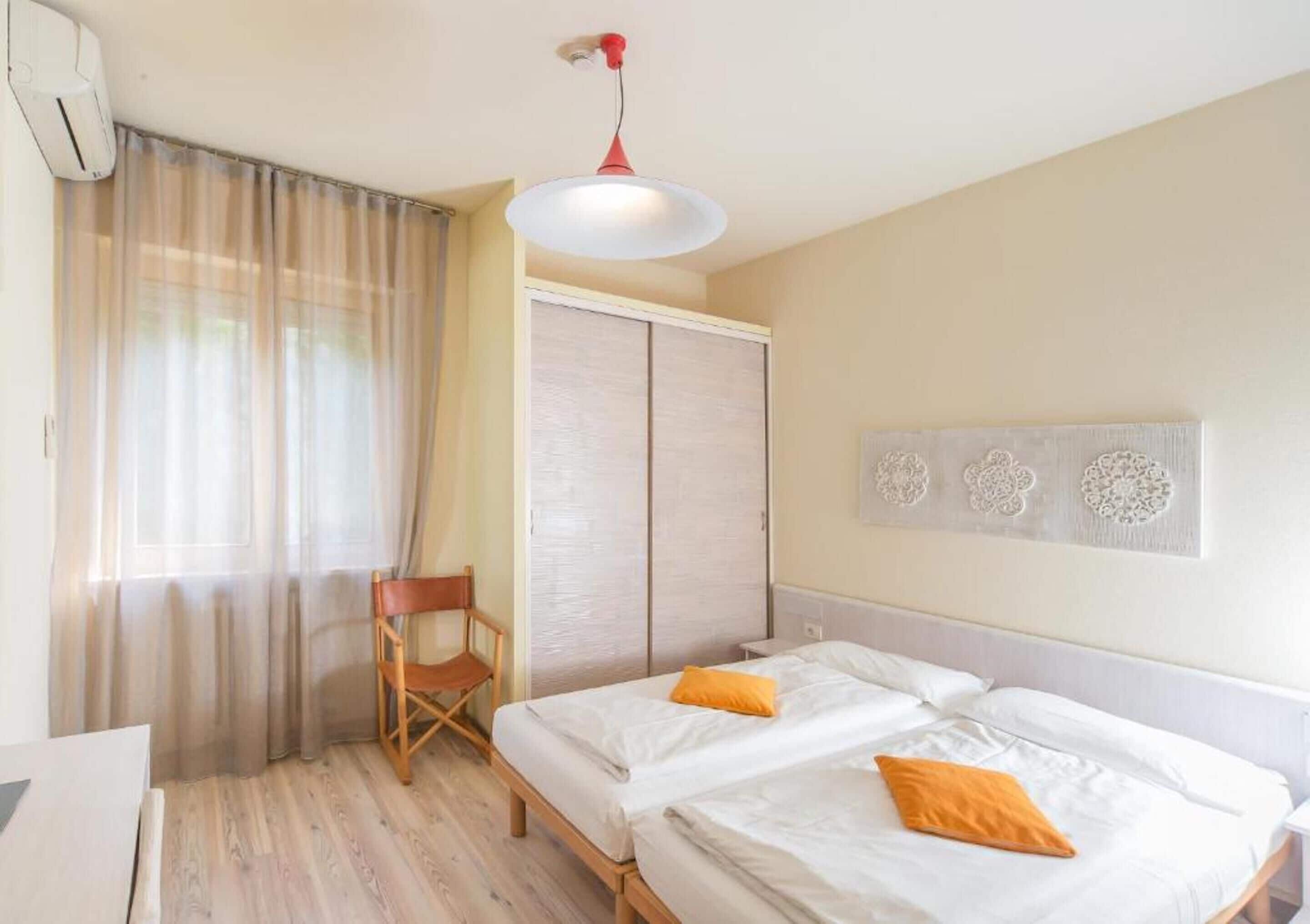 A hotel room with two beds, a chair, a wardrobe, and a ceiling light.
