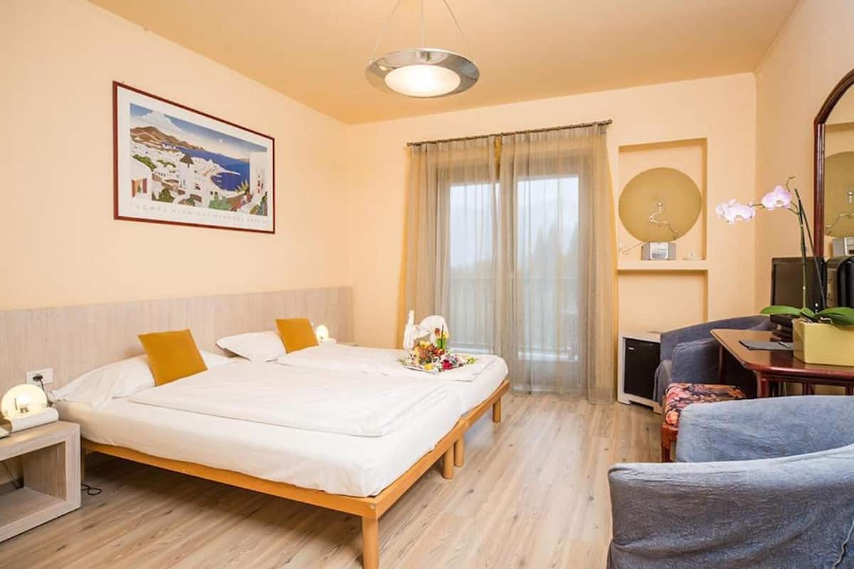 Habitación de hotel con cama, escritorio, silla, espejo y ventana con cortinas.