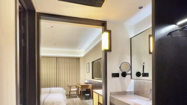 A hotel room with a bed, a desk, a bathroom with a sink and mirror, and a shower area. - Baizhao Mountain Hotel (Anlu)