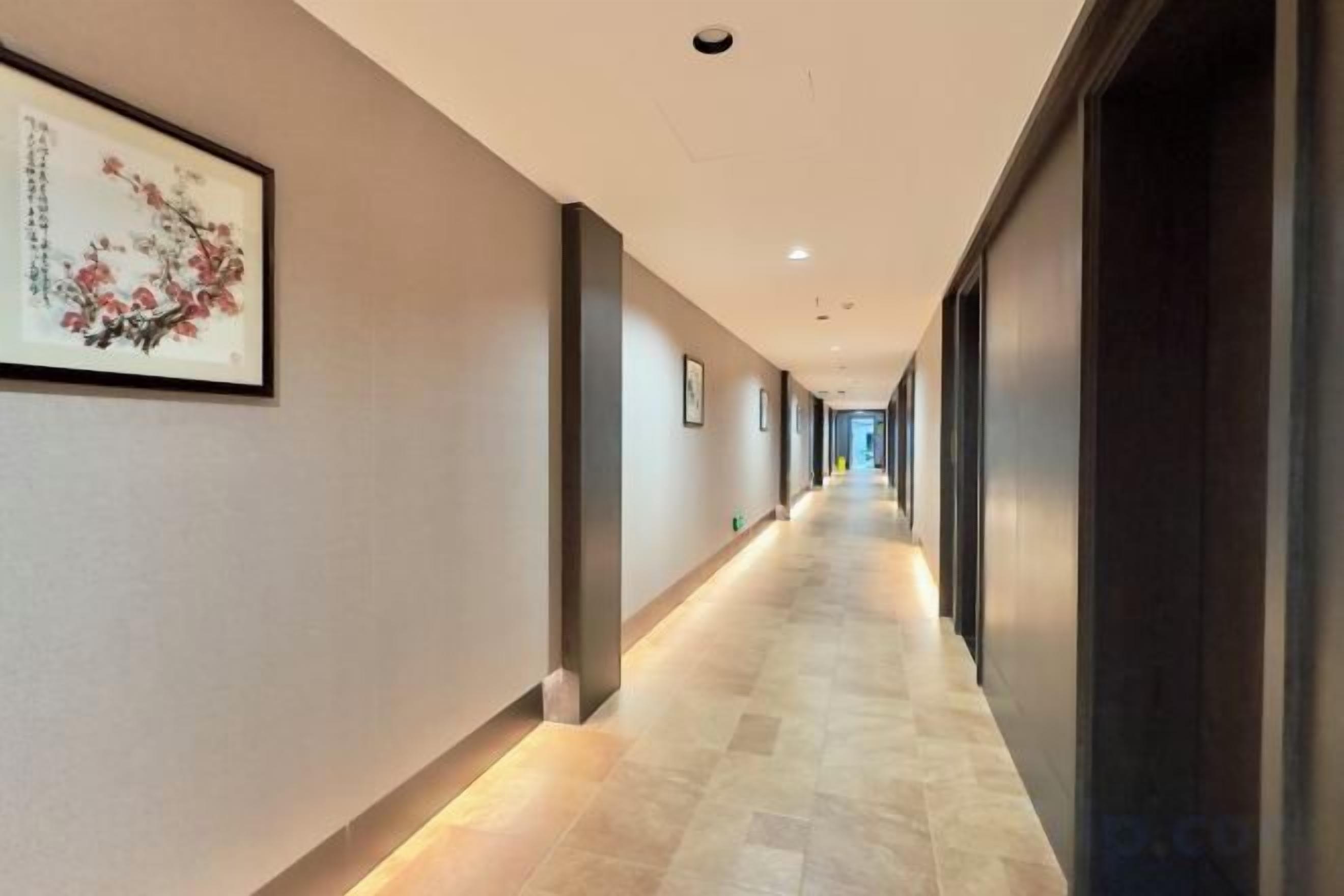 A long, narrow hallway with a tiled floor, framed artwork on the walls, and a dark door on the right.