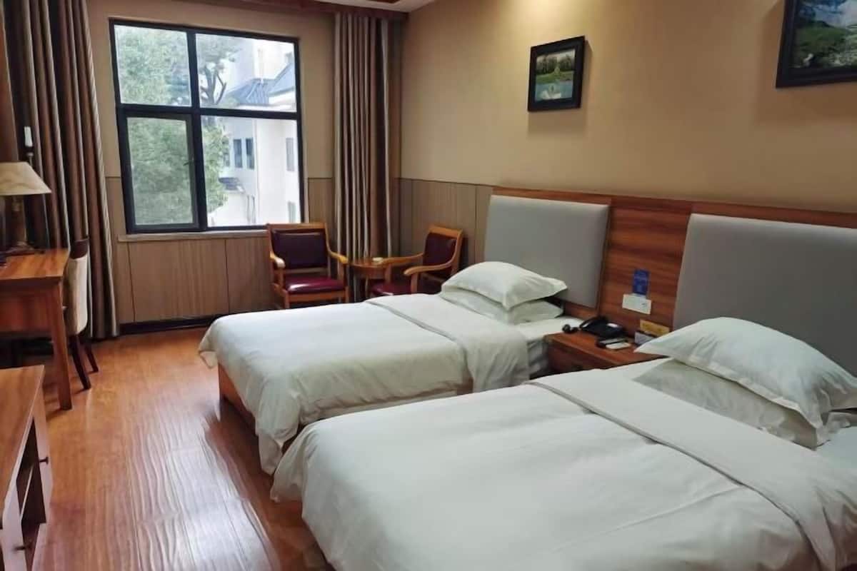Ein Hotelzimmer mit zwei Betten, einem Schreibtisch, einem Stuhl, einem Fenster mit Vorhängen und einem Bild an der Wand.