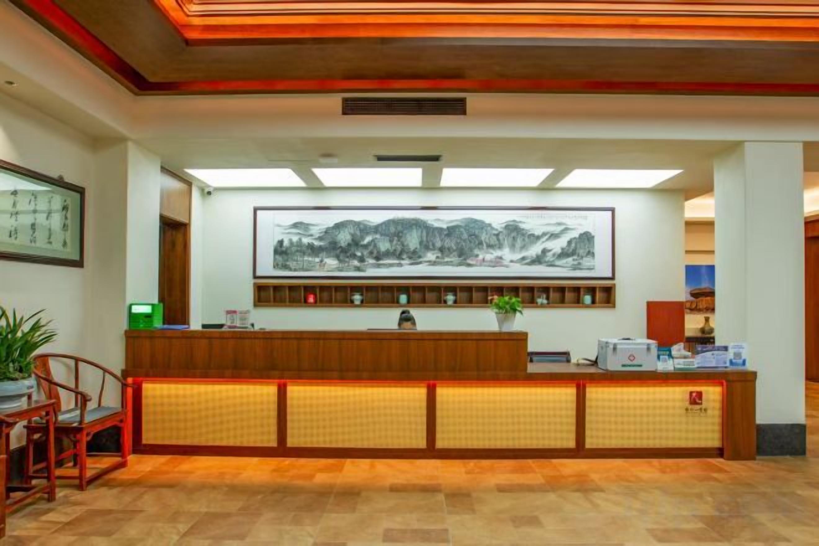 A reception desk with a large framed artwork above it, a plant on the desk, and a seating area with chairs to the left.