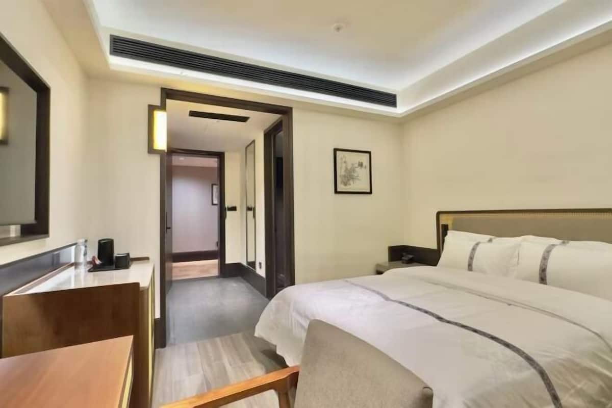 Ein Hotelzimmer mit Bett, Nachttisch und Schreibtisch mit Stuhl. Eine Tür führt in einen weiteren Raum.