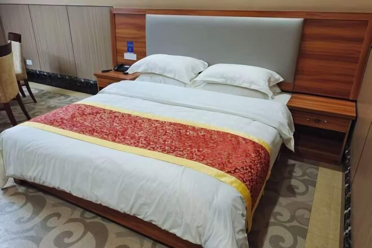 Ein Hotelzimmer mit einem großen Bett, einem hölzernen Kopfteil, einem Nachttischchen mit Telefon und einem Sessel.