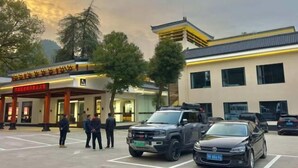 A hotel entrance with a traditional architectural style, a parking area with several vehicles, and a group of people standing near the entrance. - Baizhao Mountain Hotel (Anlu)