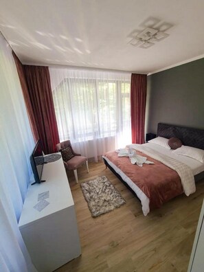 A bedroom with a bed, a desk, a chair, and a window with curtains. - Baile Puturoasa (Vama)