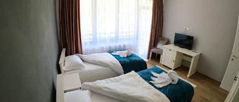 A hotel room with two beds, a desk, a television, and a window with curtains.