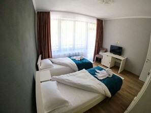 A hotel room with two beds, a desk, a television, and a window with curtains.