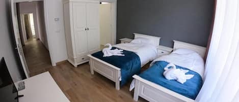 A hotel room with two beds, a wardrobe, a desk, and a television.