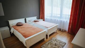 Un lit double avec une tête de lit blanche et une couverture rose, une petite table de chevet et un tapis en fourrure sur un plancher en bois.
