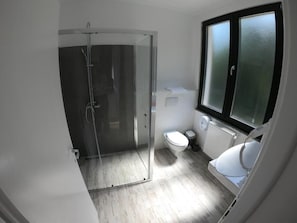 A bathroom with a glass shower enclosure, a toilet, and a window. - Baile Puturoasa (Vama)