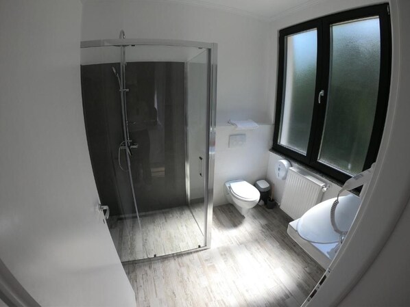 A bathroom with a glass shower enclosure, a toilet, and a window.