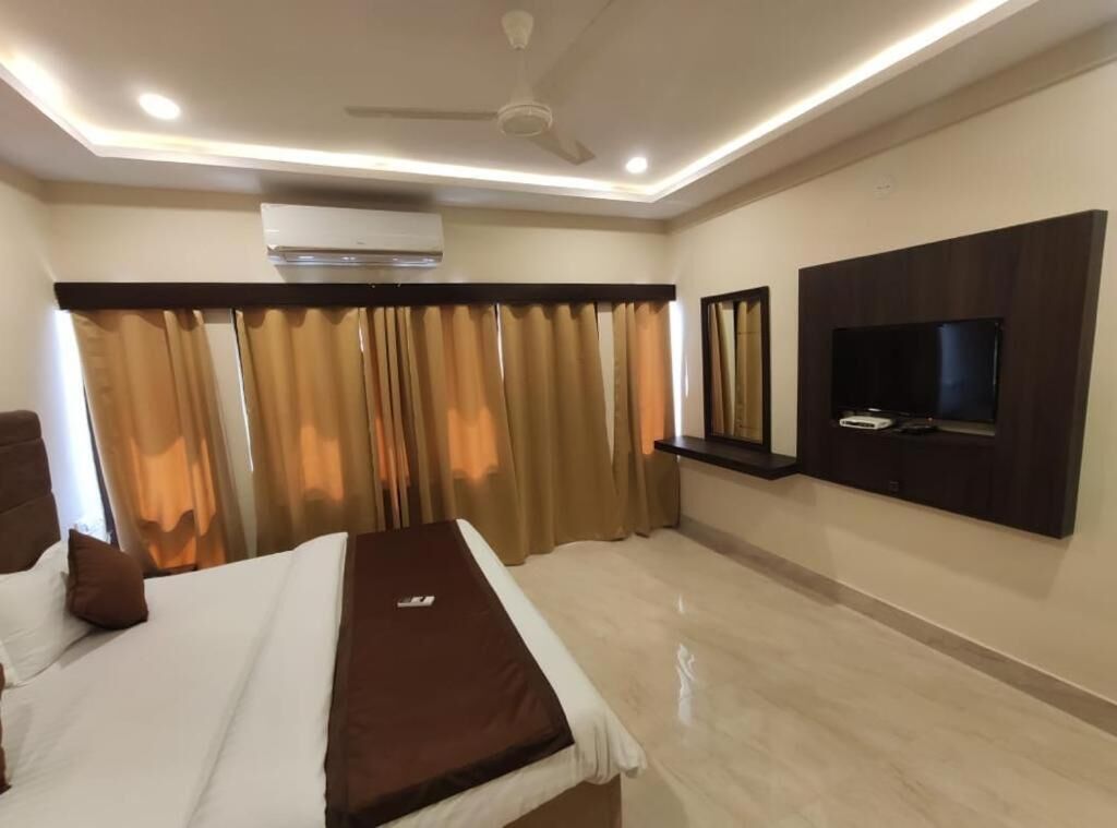 A hotel room with a bed, a flat-screen TV mounted on the wall, and a ceiling fan.
