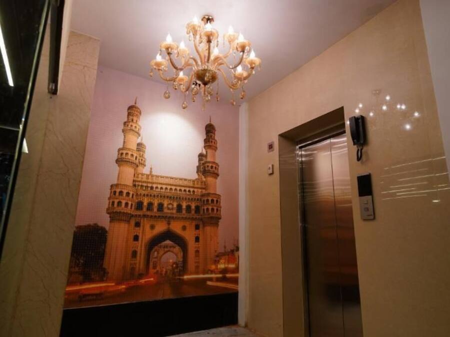A hallway with a large mural of a historic building, an elevator, and a chandelier.