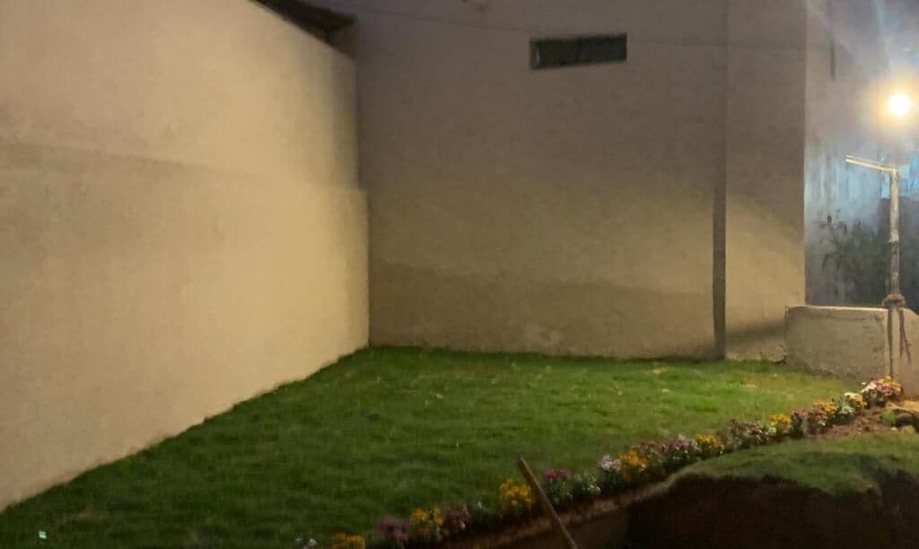 Un pequeño espacio exterior cercado, con césped y un parterre de flores.
