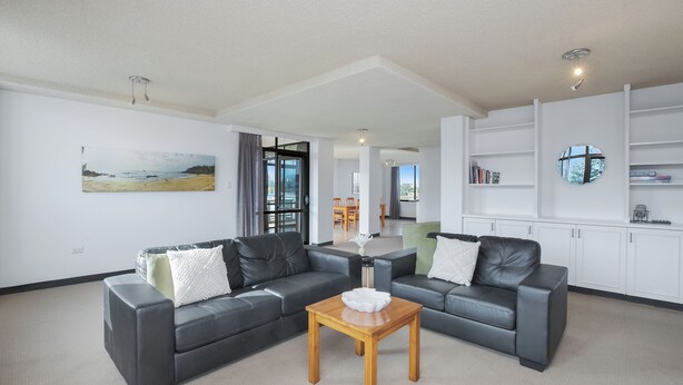 A modern living room with two grey leather sofas, a wooden coffee table, and a painting of a beach scene. - Fountain Court 25 - Spacious Unit with Ocean Views (Port Macquarie)