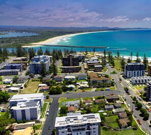 An aerial view of a coastal residential area with modern buildings, a beach, and a rocky coastline.