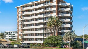 A multi-story building with balconies, a sign reading 'Fountain Court,' and a palm tree in the foreground. - Fountain Court 25 - Spacious Unit with Ocean Views (Port Macquarie)