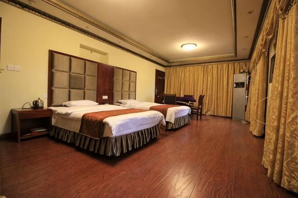 A hotel room with two beds, a wardrobe, a desk, and a television.
