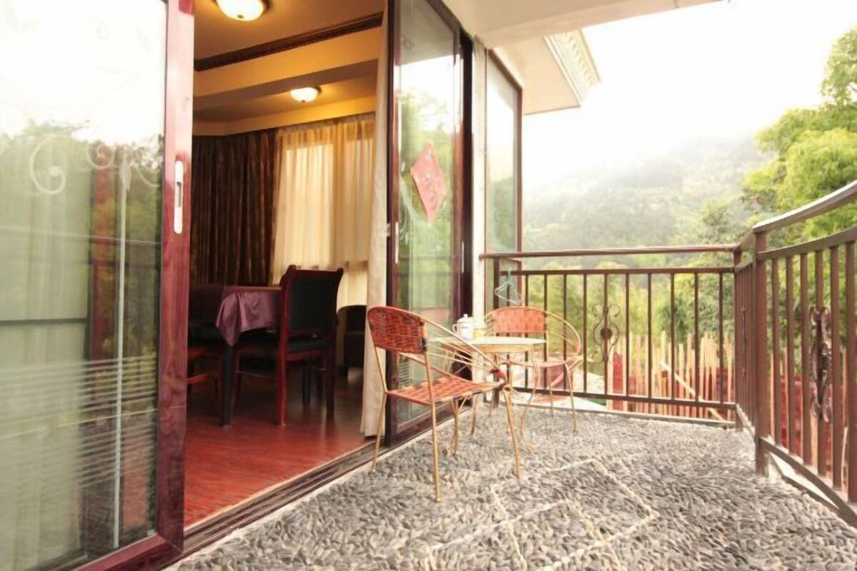 A balcony with a table and chairs, a view of greenery, and a red carpet.