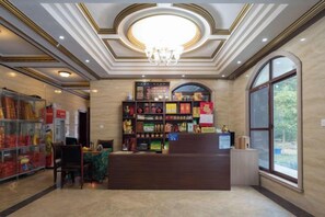 A hotel lobby with a reception desk, a chandelier, and a large window.